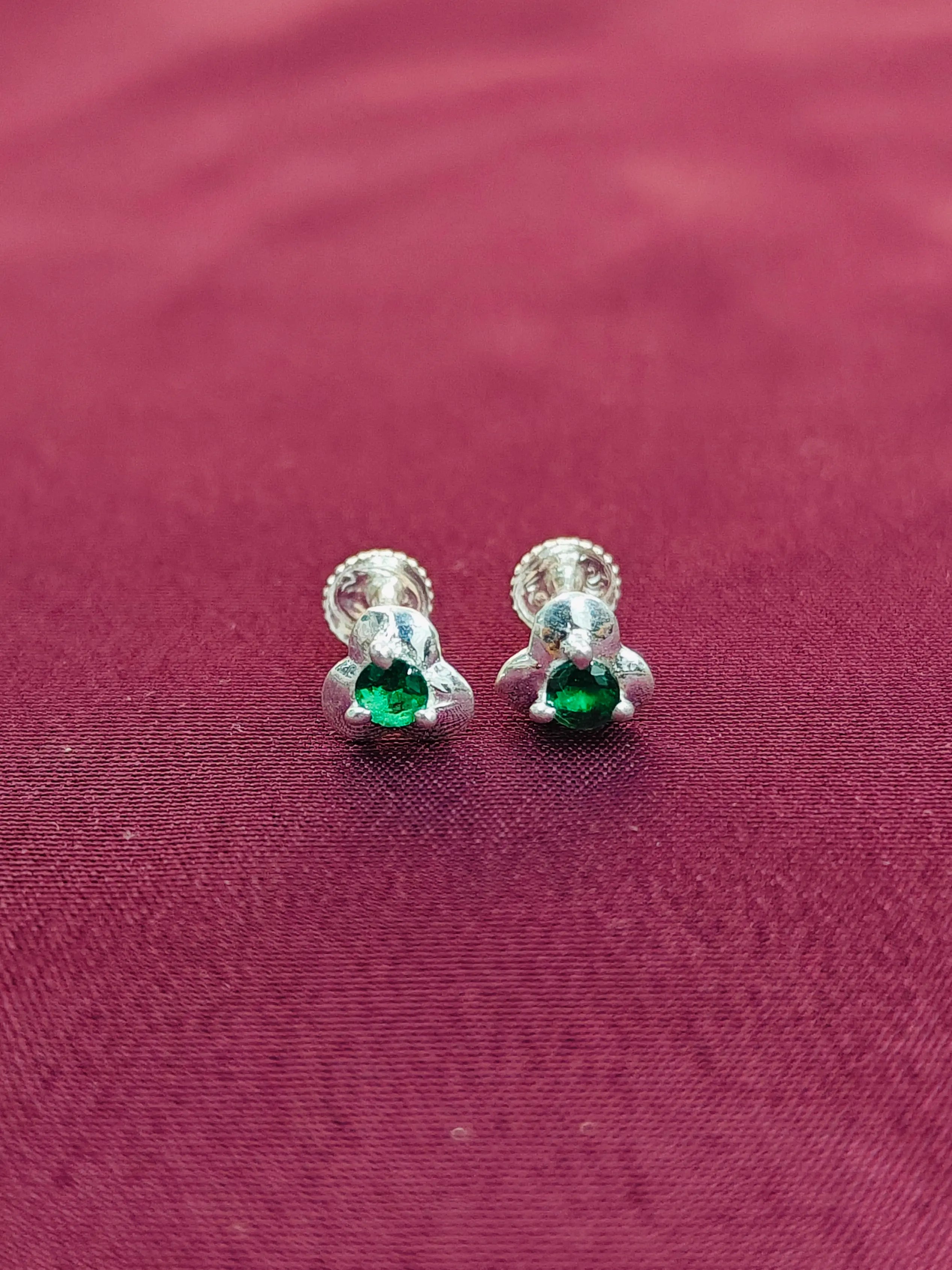 Silver earrings with green gemstones on a maroon fabric background